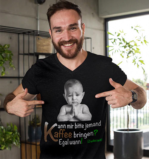 Mann mit schwarzem V-Ausschnitt-T-Shirt, auf dem ein lustiges Baby-Motiv zu sehen ist. Das Motiv zeigt ein Baby, das verschmitzt schaut, begleitet von dem Spruch: 'Kann mir bitte jemand Kaffee bringen? Egal wann!' Das Design kombiniert Humor mit Alltagssituationen und spricht moderne Streetwear-Fans an.