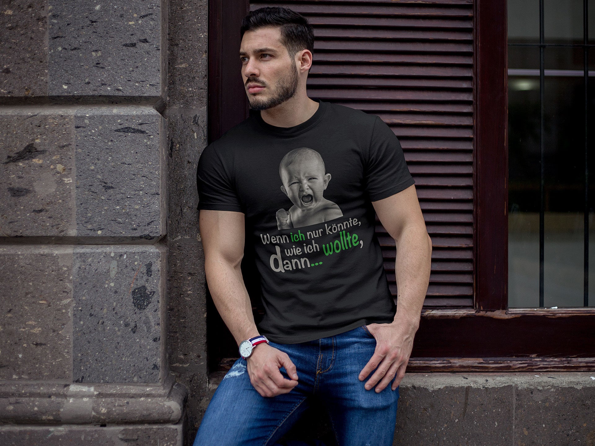 Männliches Model in lässiger Pose vor einer urbanen Kulisse, trägt ein schwarzes T-Shirt mit einem humorvollen Baby-Motiv und dem Spruch „Wenn ich nur könnte, wie ich wollte, dann…“. Ideal für Streetwear-Stil, der Persönlichkeit und Humor verbindet. Perfekt für Promotions und Online-Shop-Darstellungen.